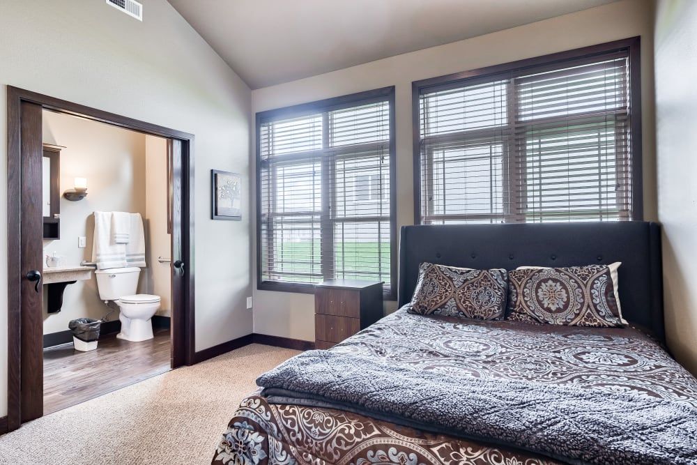 A cozy bedroom with large windows, featuring a comfortable bed and an adjoining bathroom.