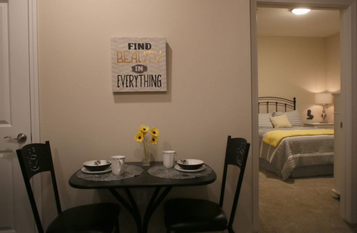 A cozy dining area with a small table set for two, featuring wall art and a glimpse into a bedroom.