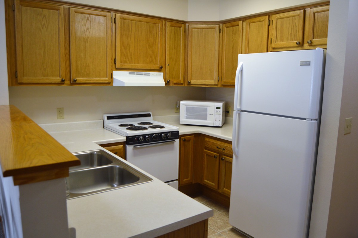 A modern kitchen with wooden cabinets, a refrigerator, stove, microwave, and a double sink.