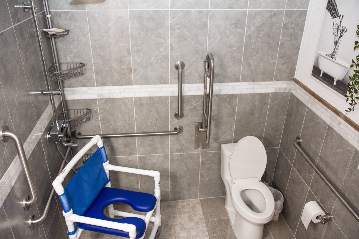 An accessible bathroom featuring a shower chair and safety grab bars.