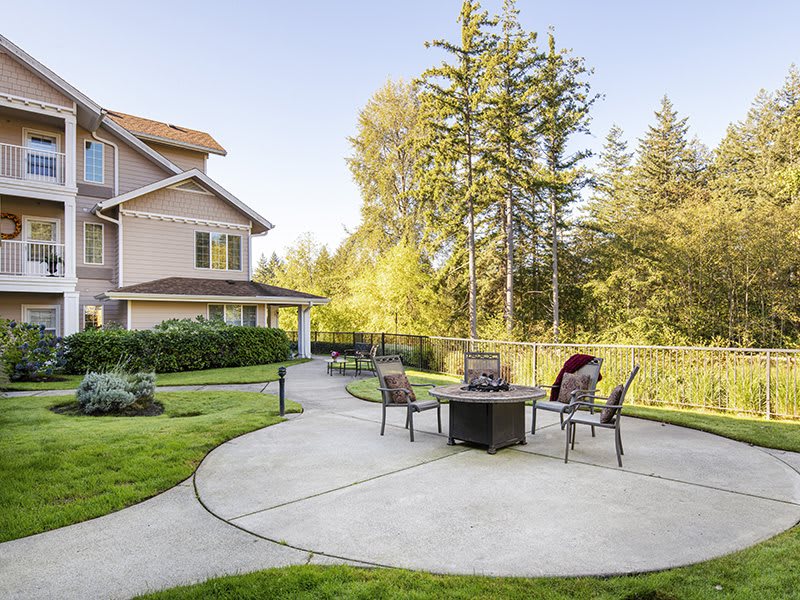 A serene backyard patio with chairs and a fire pit surrounded by greenery.