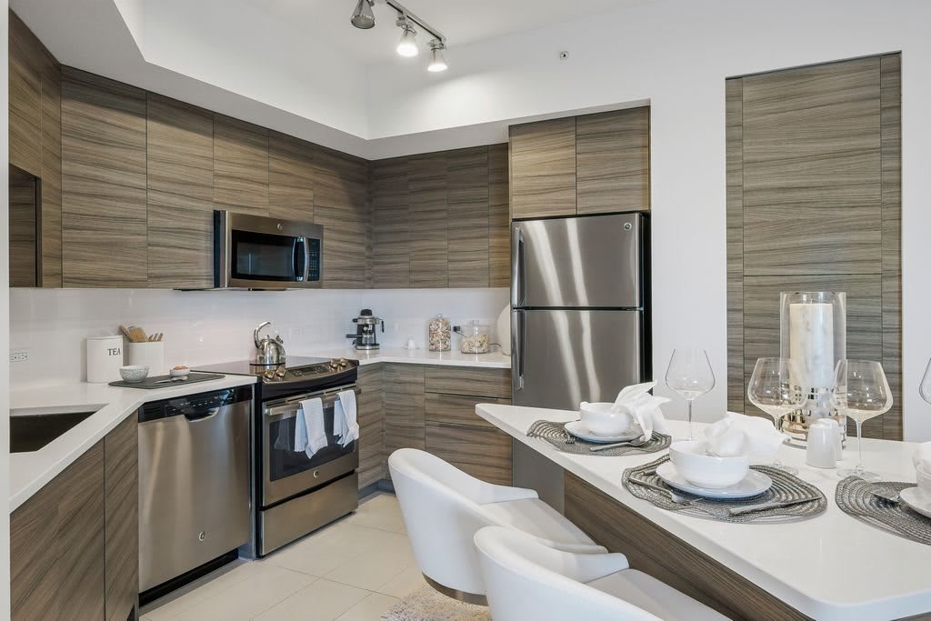 A modern kitchen featuring stainless steel appliances and wood cabinetry with a cozy bar seating area.