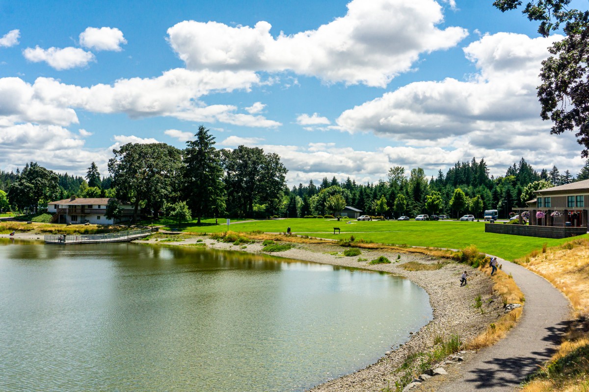 A peaceful lakeside landscape with lush greenery and fluffy clouds in the sky.