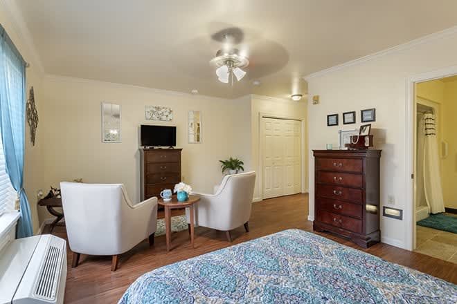 A cozy bedroom with a bed, two chairs, a dresser, and a television.