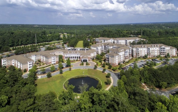 Aerial view of a large residential complex surrounded by lush greenery and featuring a central pond.