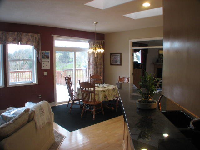 A cozy kitchen and dining area with a wooden table and chairs, featuring natural light from large windows.