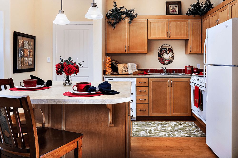 A cozy kitchen with wooden cabinets, featuring red accents and a central island adorned with flowers.
