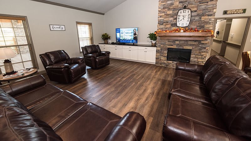 A cozy living room with leather seating, a large TV, and a stone fireplace.