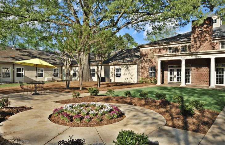 A scenic courtyard with a landscaped garden and large tree in front of a building.
