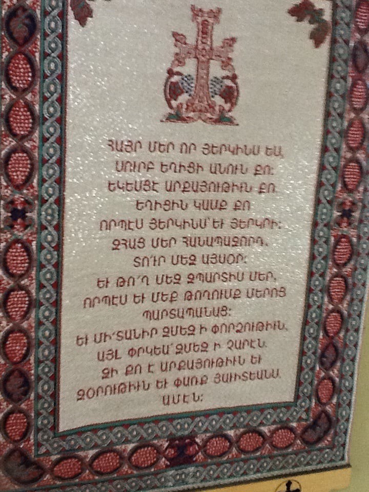 An ornate textile featuring a religious or cultural Armenian inscription with decorative borders.