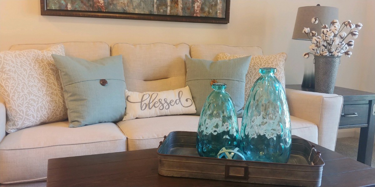 A cozy living room setup featuring a beige sofa with decorative pillows and a wooden coffee table adorned with blue glass vases.