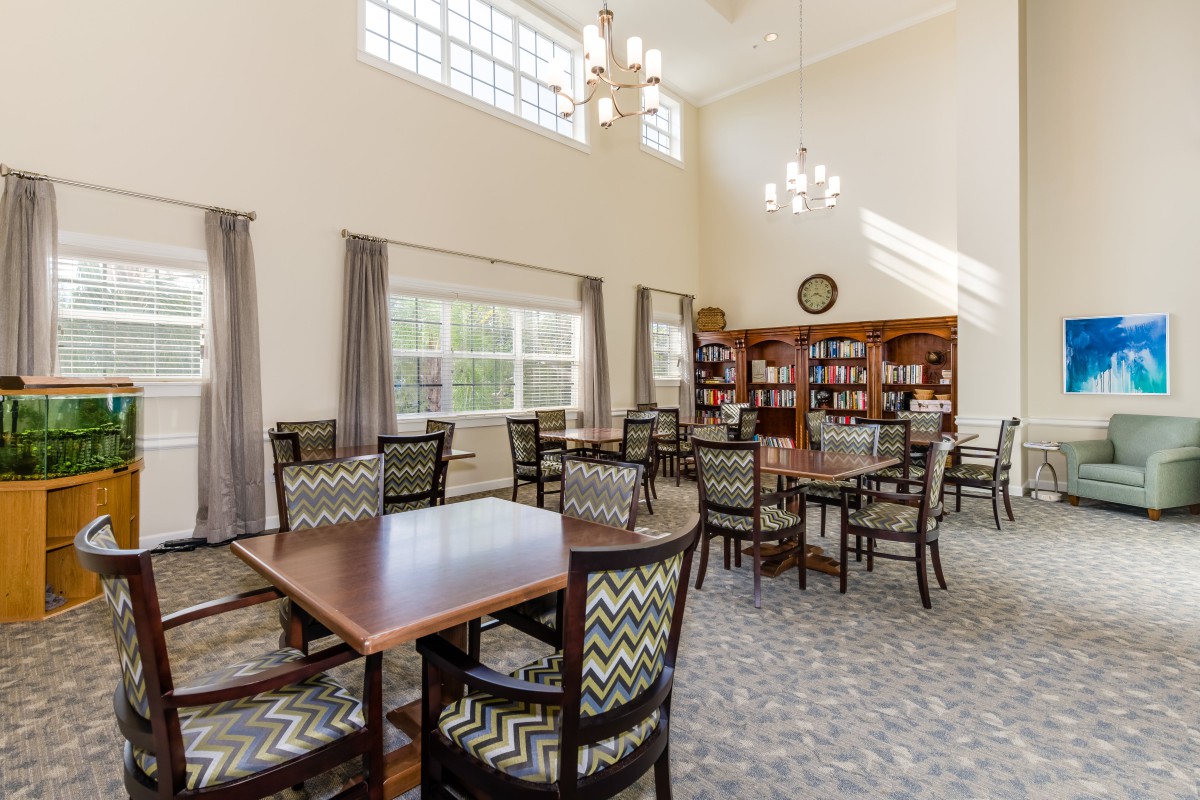 A bright library room with tables and chairs, illuminated by natural light from large windows.