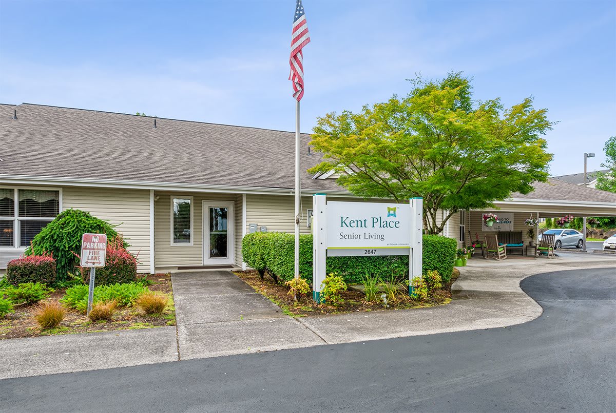 A one-story building with an American flag and a sign reading 'Forest Place Apartments' near the entrance, surrounded by well-maintained landscaping.