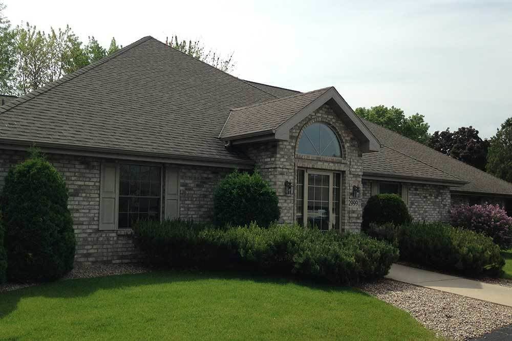 A stone-faced residential house with well-maintained landscaping and a peaked roof.