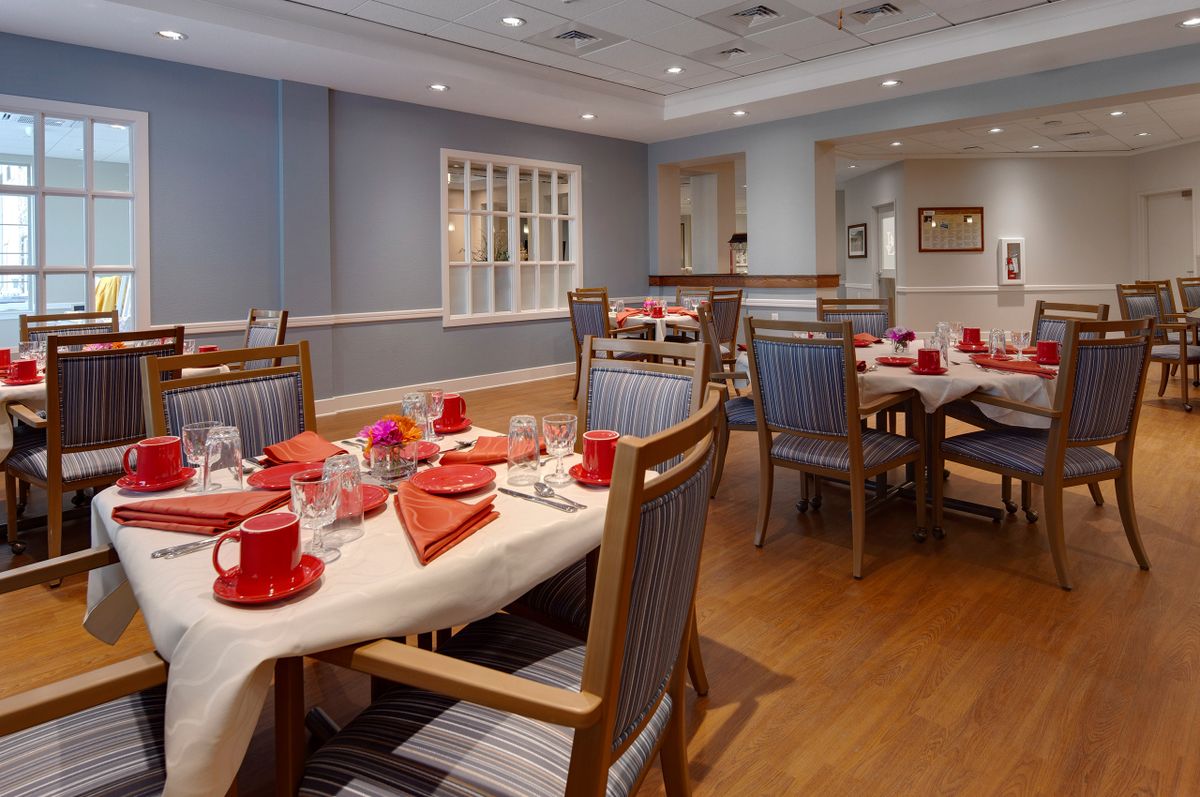 A cozy dining room with neatly set tables, featuring red tableware and comfortable seating.