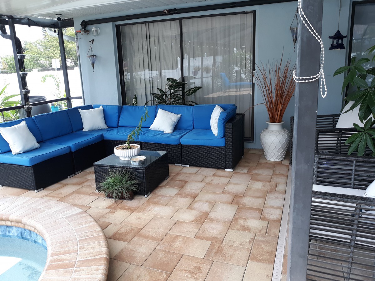 A cozy outdoor patio with a blue cushioned sofa and a small coffee table surrounded by decorative plants.