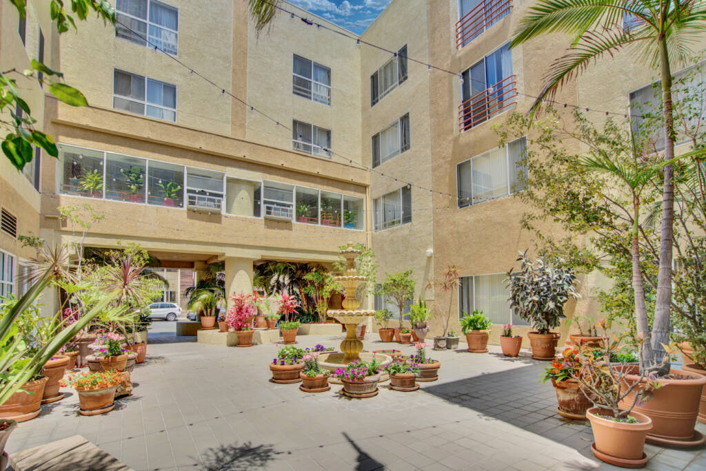 A sunny courtyard of an apartment building adorned with various potted plants.