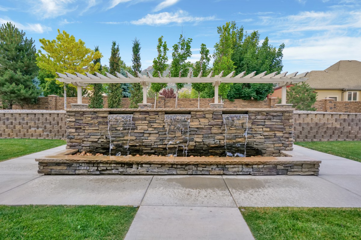 A stone fountain with cascading water surrounded by a lush garden and pathway.
