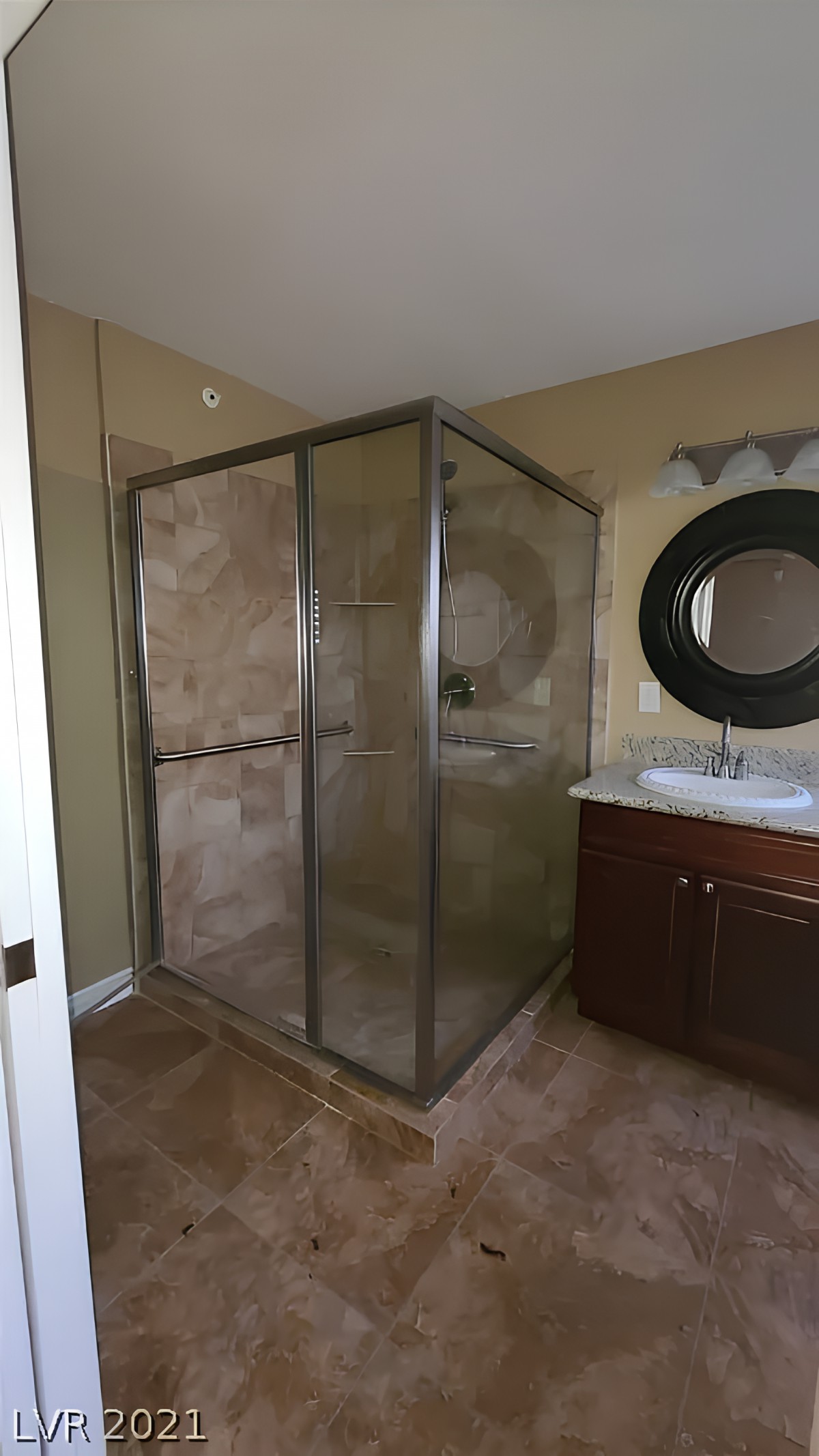 A modern bathroom featuring a glass-enclosed shower, a sink with a mirror above, and tiled flooring.