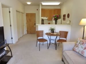 A cozy apartment living space featuring a small table with two chairs, a sofa, and an open view into the kitchen.