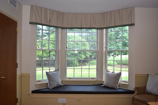 A cozy bay window with a seating area, adorned with soft pillows and curtains, inviting natural light into the room.