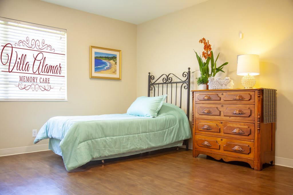 A cozy bedroom with a single bed, wooden dresser, and bright natural light.