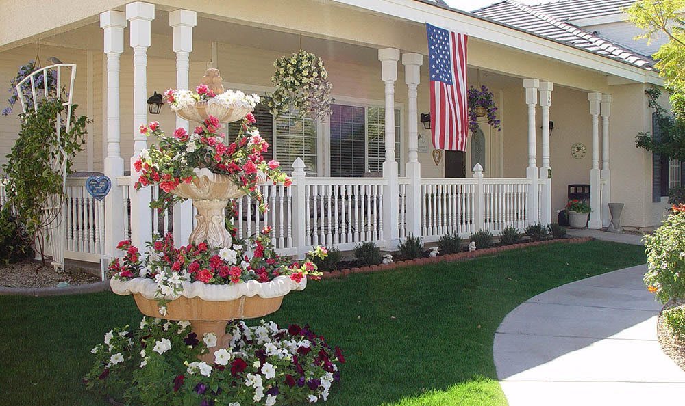 A charming house with a white porch, beautifully landscaped garden, and an American flag displayed prominently.