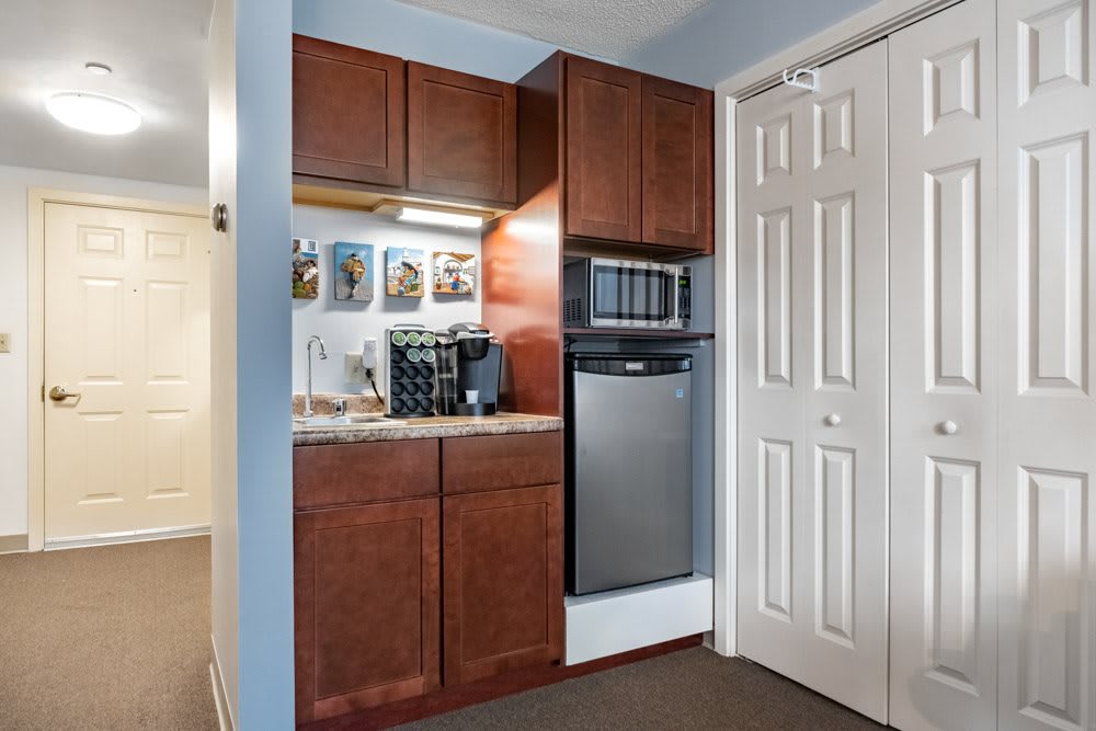 A compact kitchenette with wooden cabinets, featuring a coffee maker and microwave.