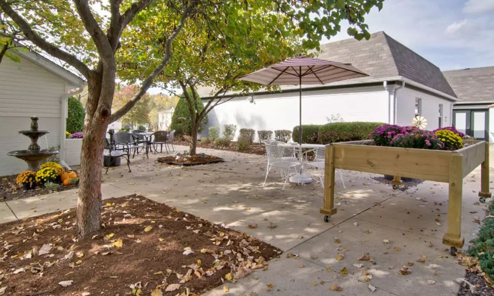 A tranquil outdoor patio area with tables, chairs, and a large umbrella under the trees.