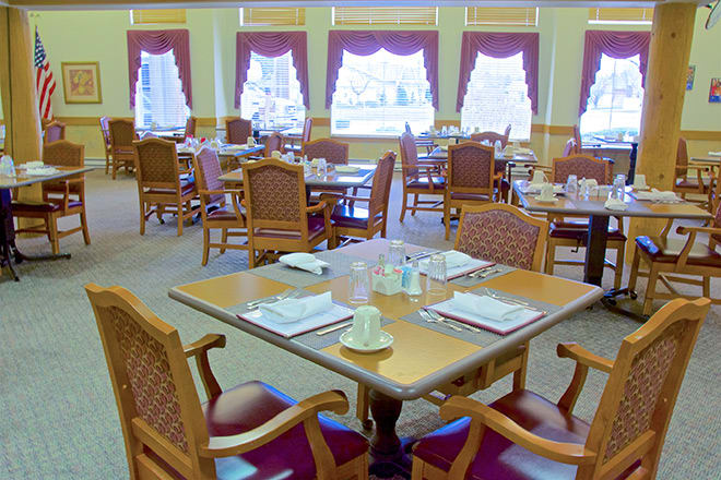 An empty dining room with neatly set tables and chairs by large windows.