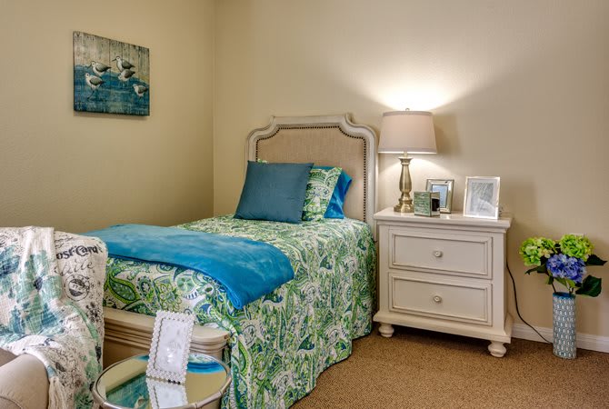 A cozy bedroom features a single bed with colorful bedding, accompanied by a nightstand and lamp for ambient lighting.