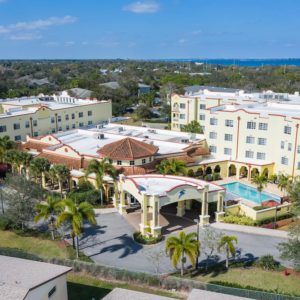Aerial view of a luxurious hotel surrounded by palm trees with the sea visible in the background.