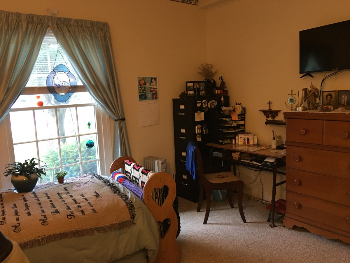 A cozy bedroom with a window, desk and chair, and a wooden dresser.