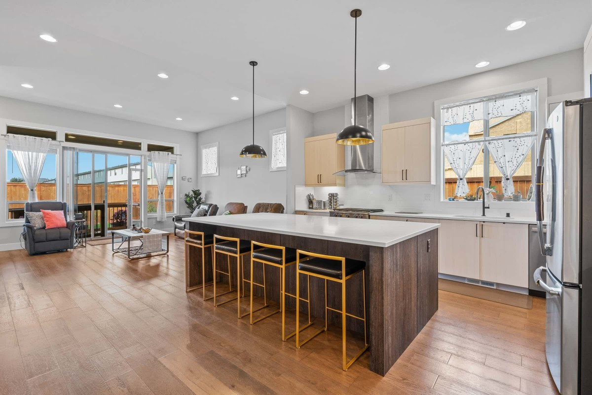 A modern kitchen with a large island, featuring pendant lighting and sleek stools.