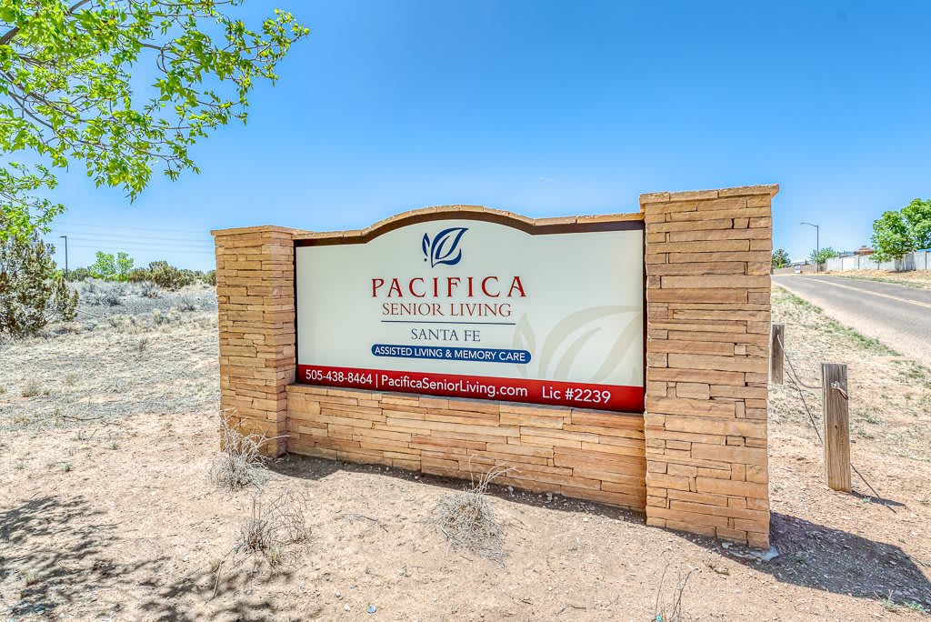 A sign for Pacifica Senior Living featuring brick pillars and a desert landscape.