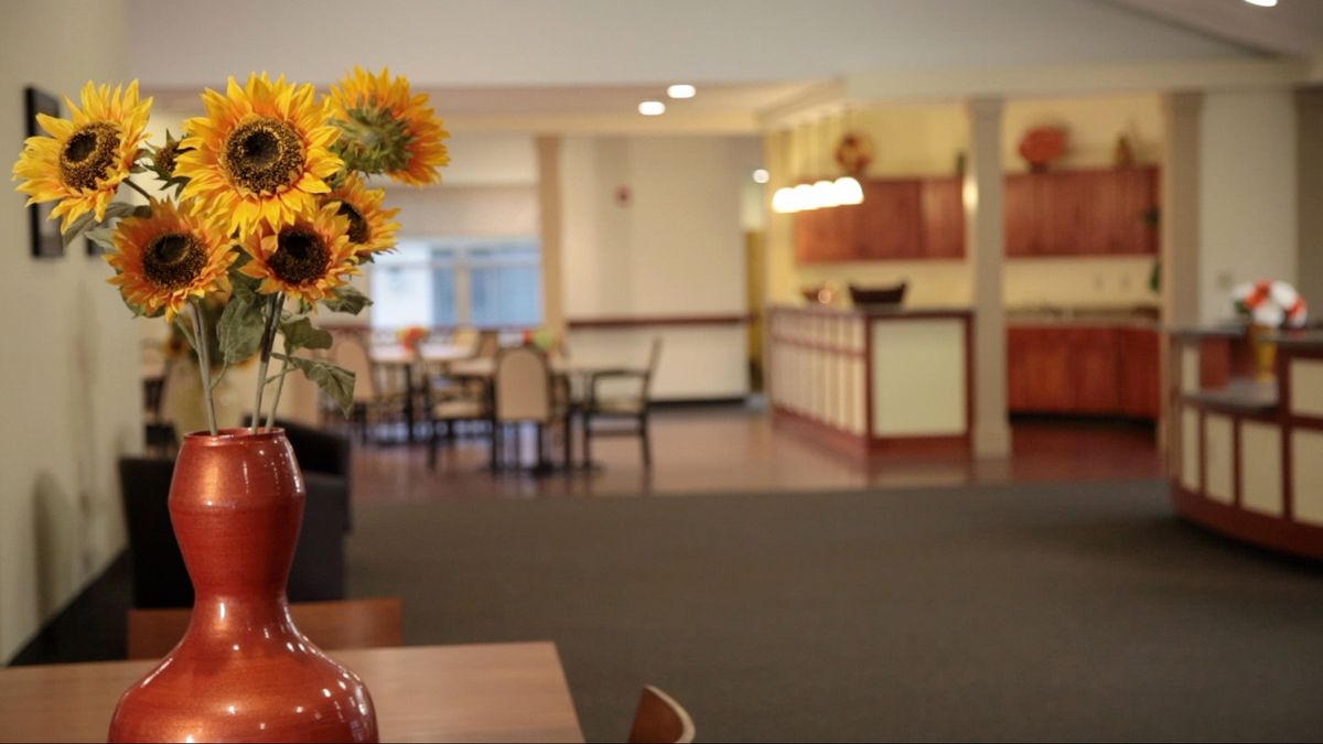 A cozy dining area with sunflowers in a vase and neatly arranged tables and chairs.