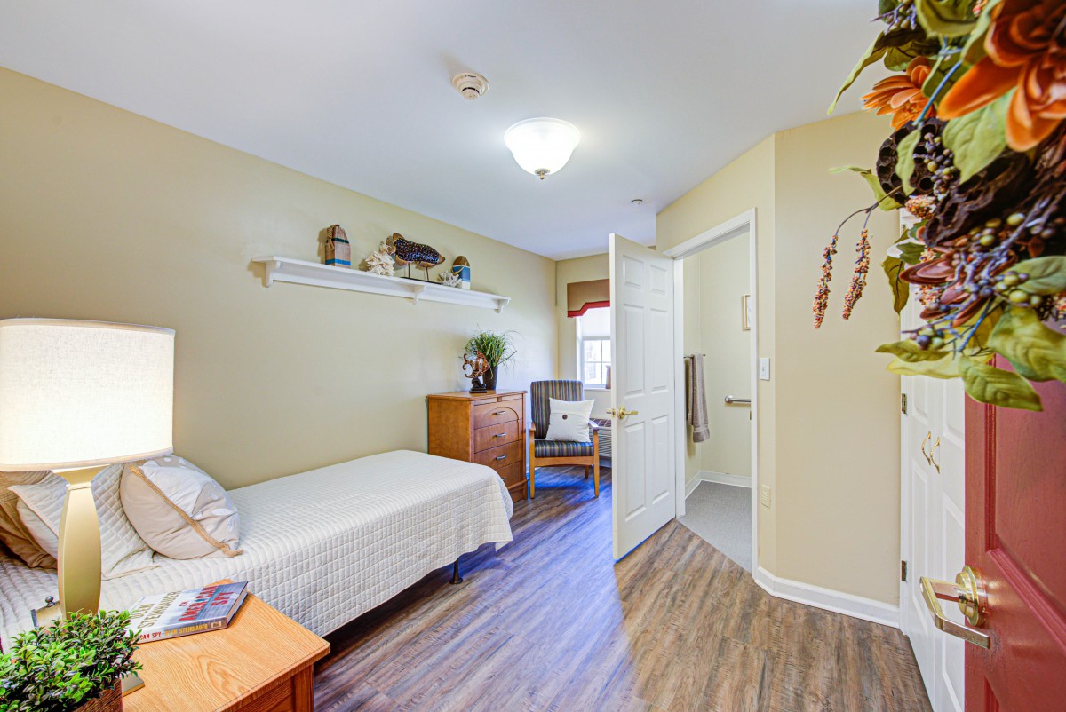 A cozy, minimalist bedroom with a single bed, wooden flooring, and bright lighting.