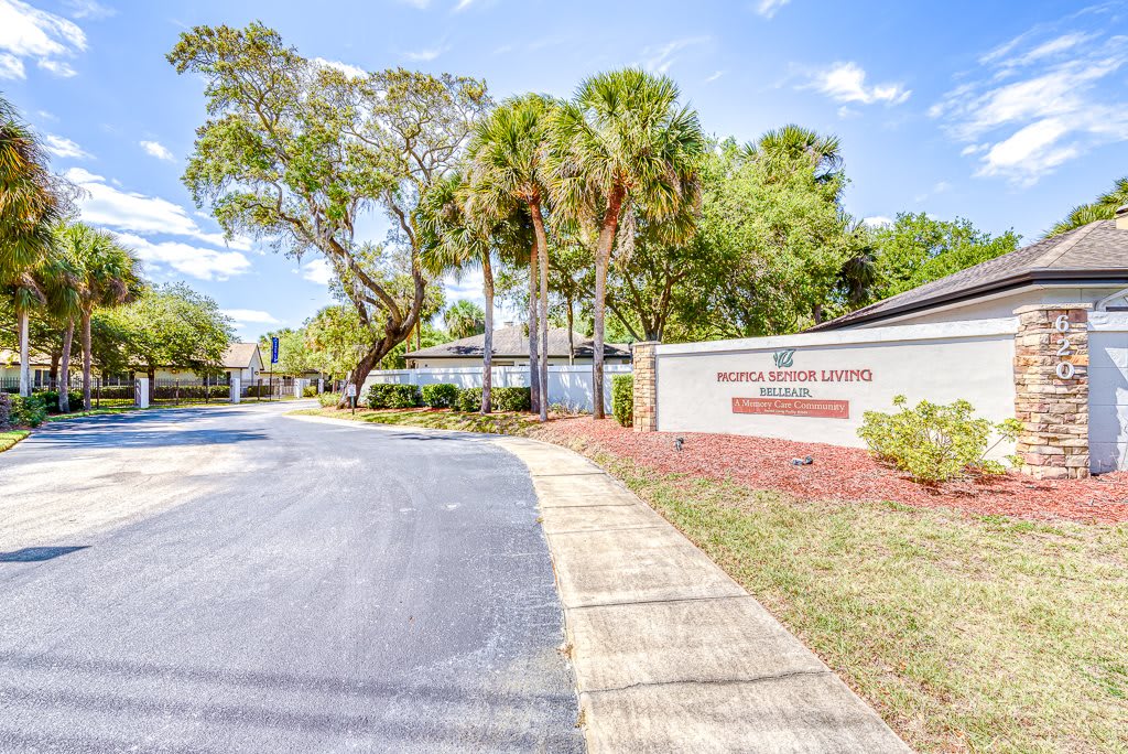 Entrance to an apartment complex with a sign and landscaping along the road.