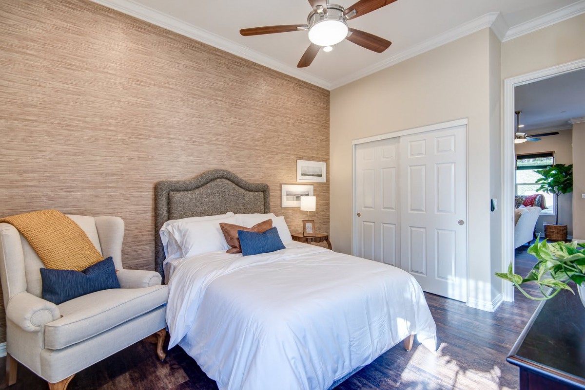 A cozy, minimalist bedroom with a comfortable bed, elegant armchair, and ceiling fan.