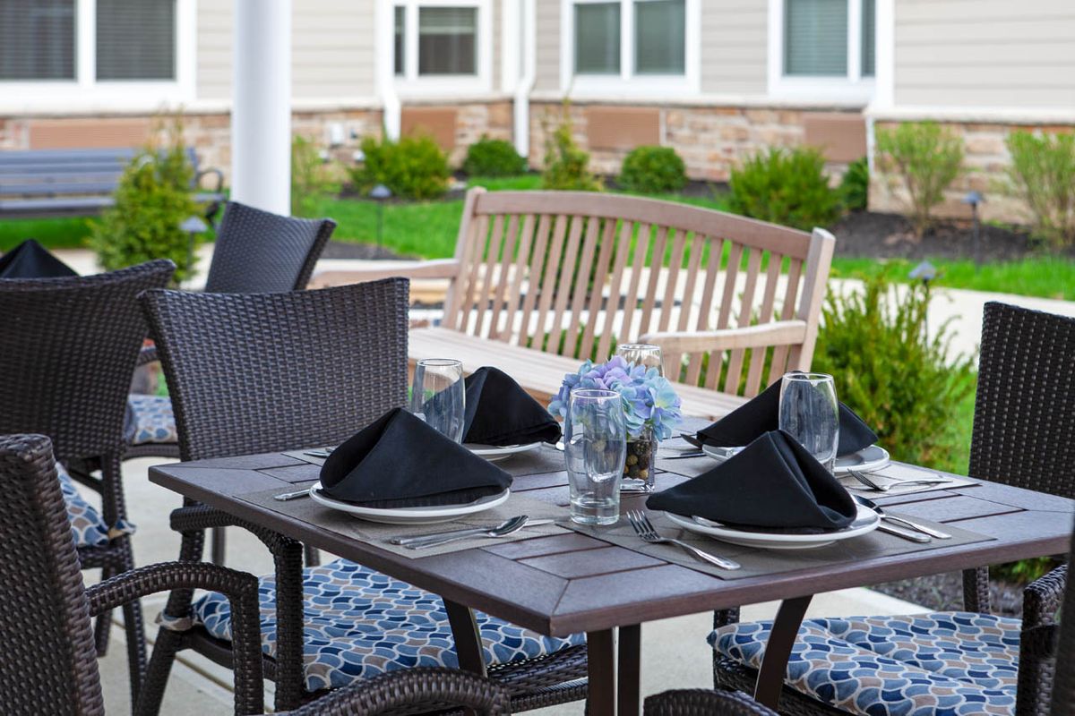 An elegantly set outdoor dining table with black napkins and patio furniture, situated in a garden setting.