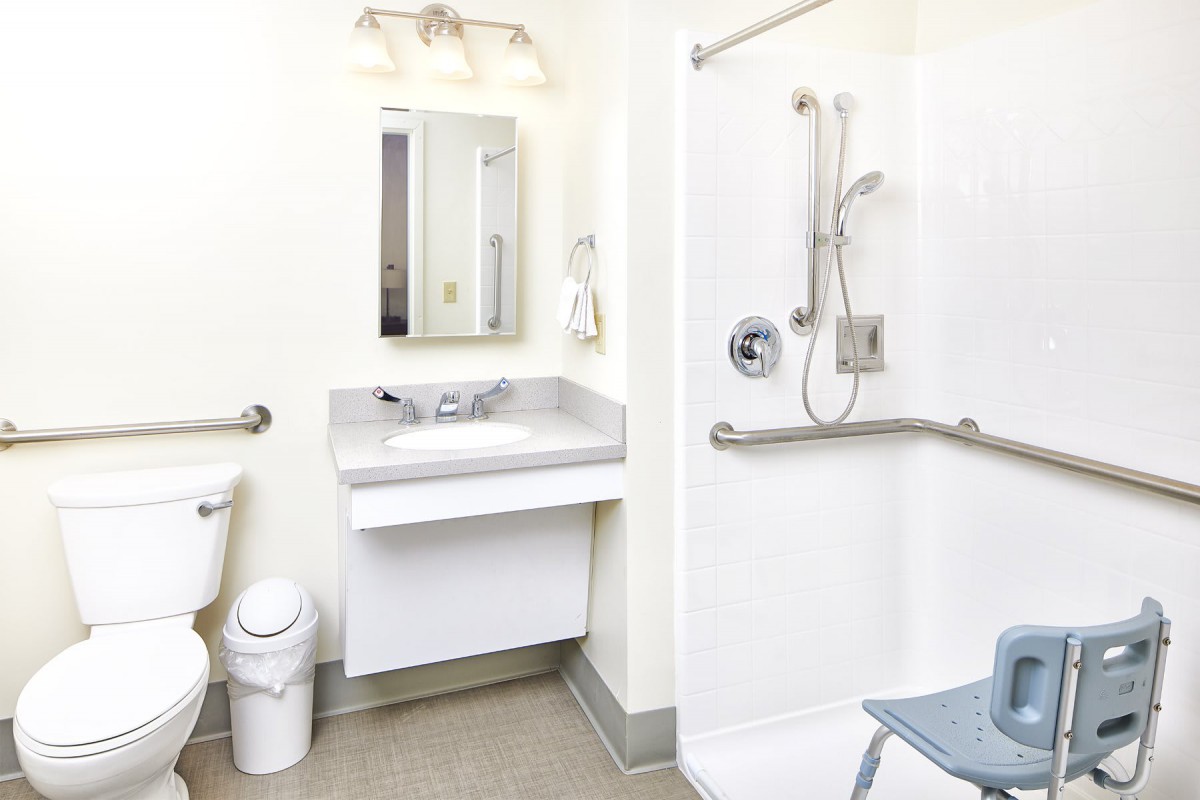 An accessible bathroom with a sink, mirror, and shower equipped with safety grab bars.