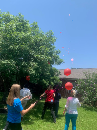 A group of people enjoying a sunny day outdoors, releasing red balloons into the sky.