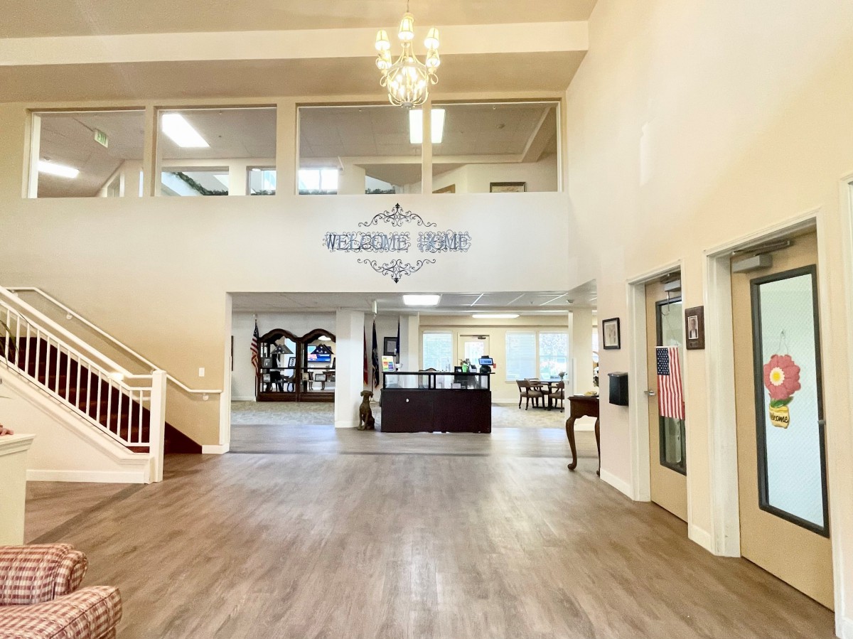 A spacious and elegant lobby with a chandelier, reception desk, elevators, and a staircase.