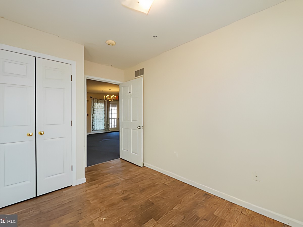 An empty room with wooden floors, white walls, and a door leading to another area.