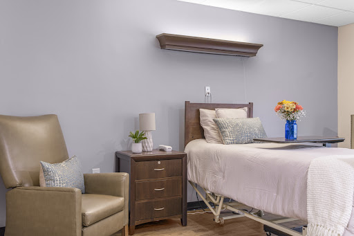 A well-organized patient room featuring a bed, nightstand with a lamp, and a comfortable chair.