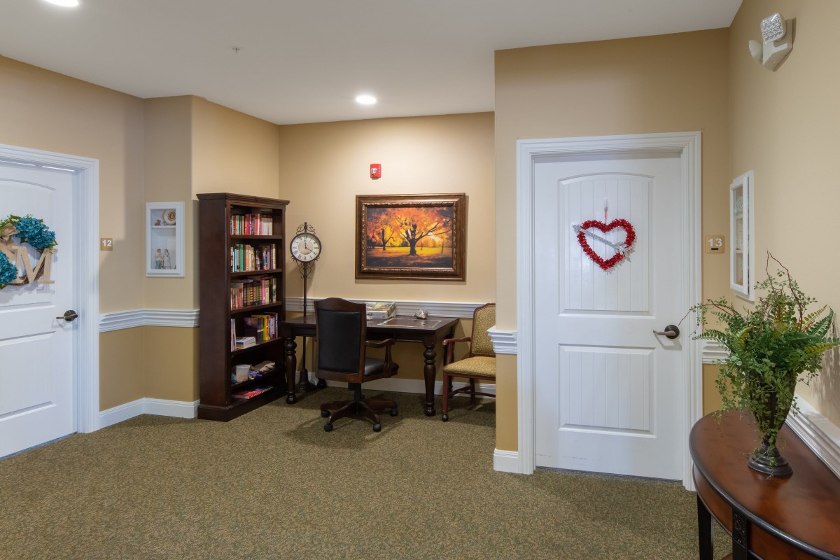 A cozy office space with a bookshelf, desk, and chair, adorned with a painting and wall decor.