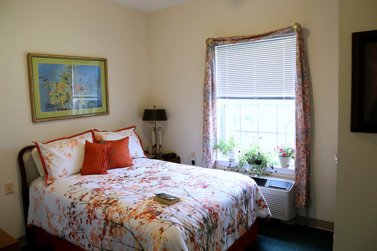 A cozy bedroom with floral bedding, decorated with plants on the windowsill and artwork on the wall.