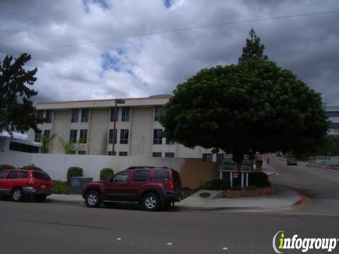 A street view of a residential building with parked cars under a cloudy sky.