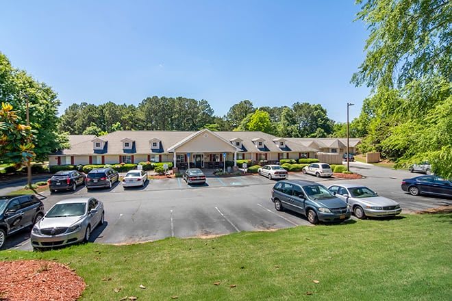A single-story building with a parking lot surrounded by trees on a clear day.