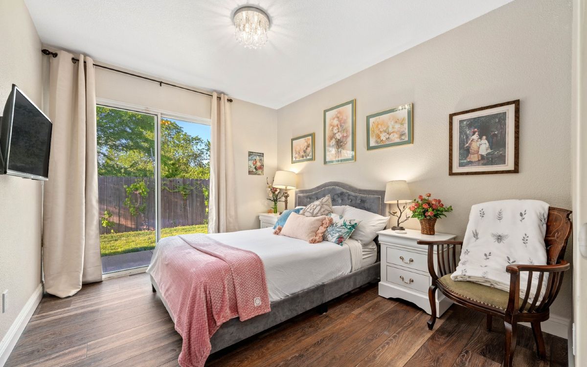 A cozy bedroom with elegant decor, featuring a comfortable bed, nightstands, and ample natural light through a sliding glass door.